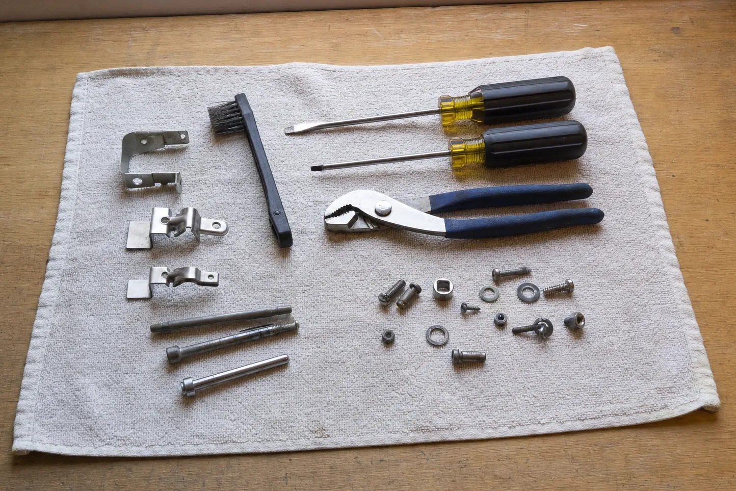 Two door hinge brackets and two clamp fittings with long shoulder bolts, laid out beside black-handled drivers and groove-joint pliers